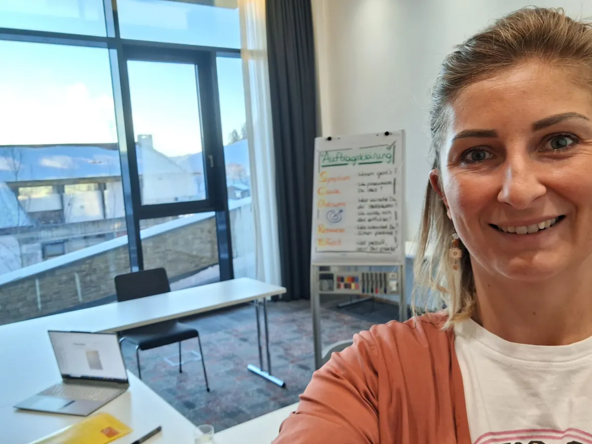 Dr. Katharina Ptack lächelt in einem vorbereiteten Trainingsraum mit Flipchart zur Auftragsklärung